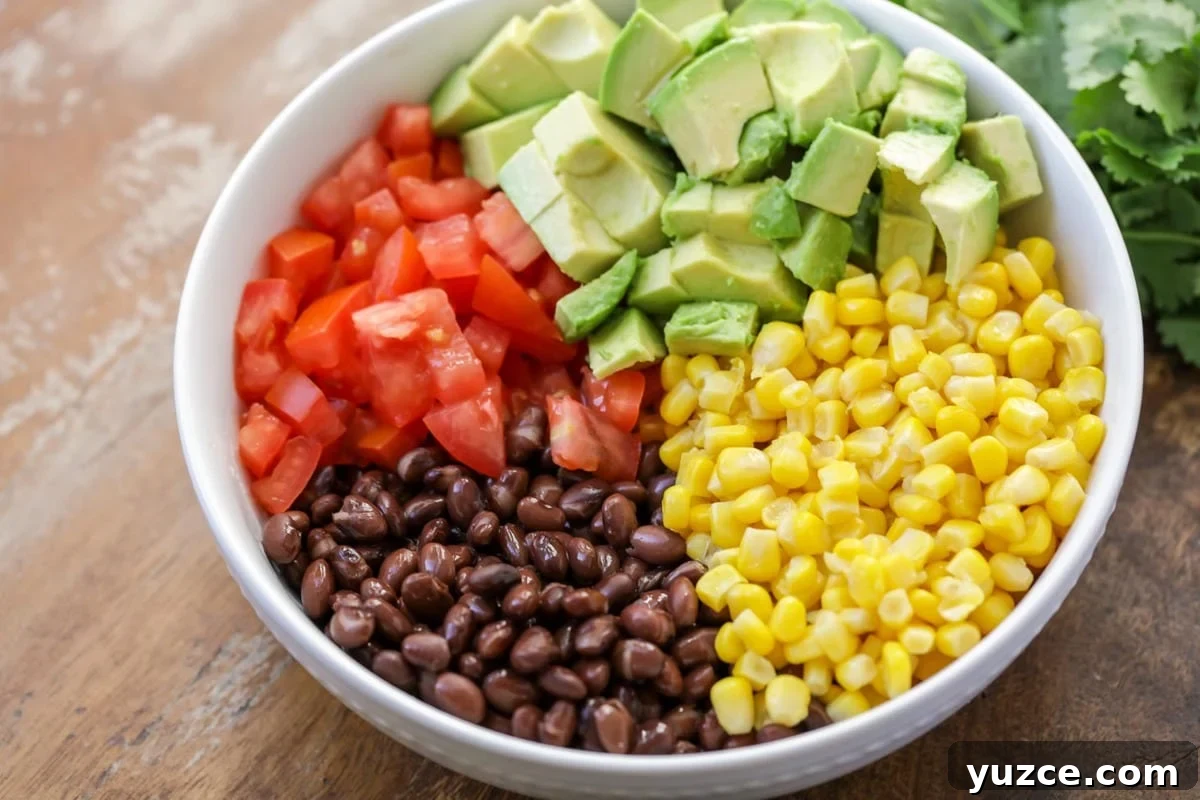 Fresh and chunky black bean corn salsa {aka Cowboy Caviar} is a favorite dip to serve with tortilla chips! Black beans, corn, tomatoes, and avocado in a white bowl.