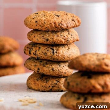Chocolate Almond Cookie Recipe with Crunchy Almonds and Cocoa 13 Stack of chocolate almond cookies showing their golden texture and chocolate flecks, with more cookies blurred in the background on a soft pink surface.