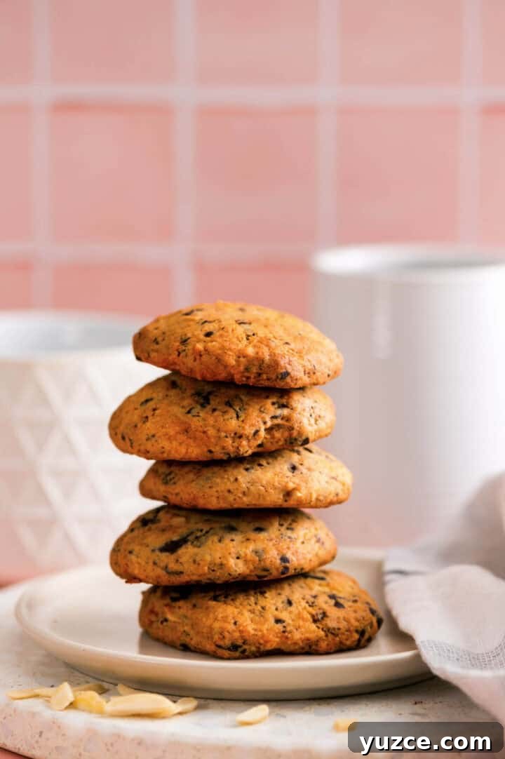 Chocolate Almond Cookie Recipe with Crunchy Almonds and Cocoa 3 Plate of stacked chocolate almond cookies on a marble surface, styled with a white napkin and soft pink background.