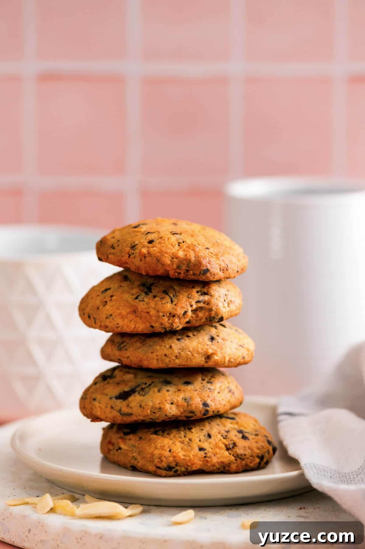 Chocolate Almond Cookie Recipe with Crunchy Almonds and Cocoa 8 Plate of stacked chocolate almond cookies on a marble surface, styled with a white napkin and soft pink background.