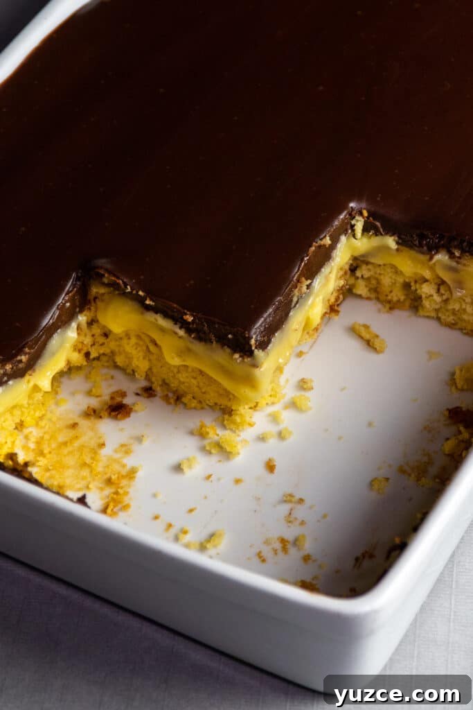 Boston Cream Pie Cake from a Box Mix — Quick Layered Dessert 3 Boston cream pie cake in a white baking dish with pieces cut out to show the custard filling.