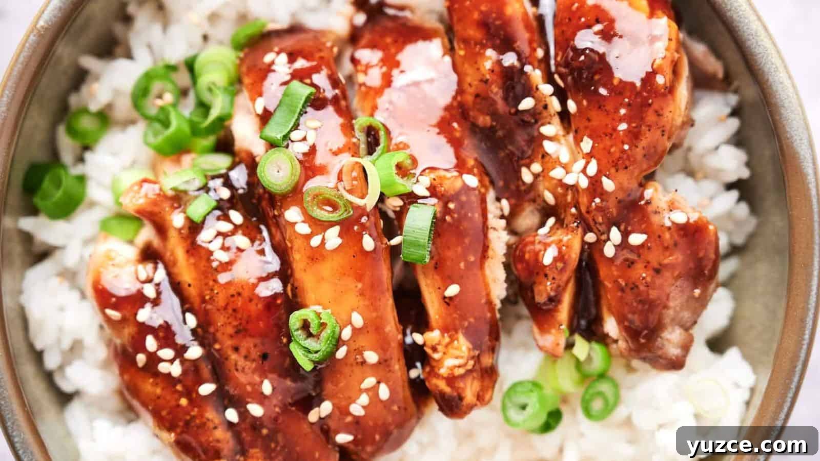 A bowl of white rice topped with glazed chicken and garnished with green onions and sesame seeds.