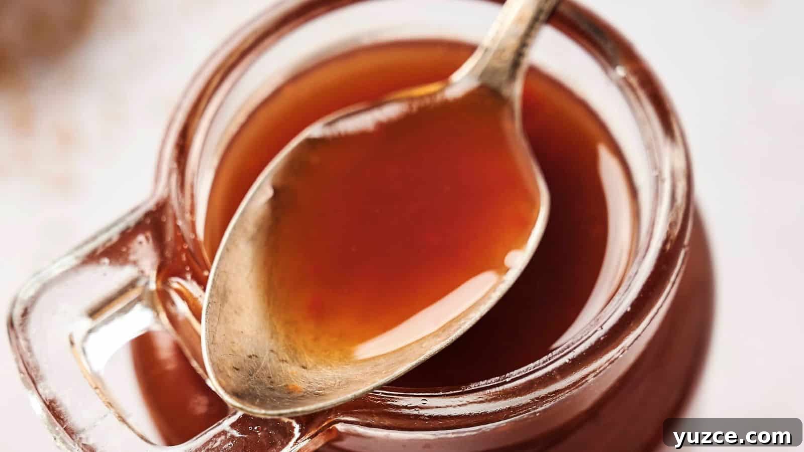 A spoon rests inside a glass jar filled with a thick, brown liquid.