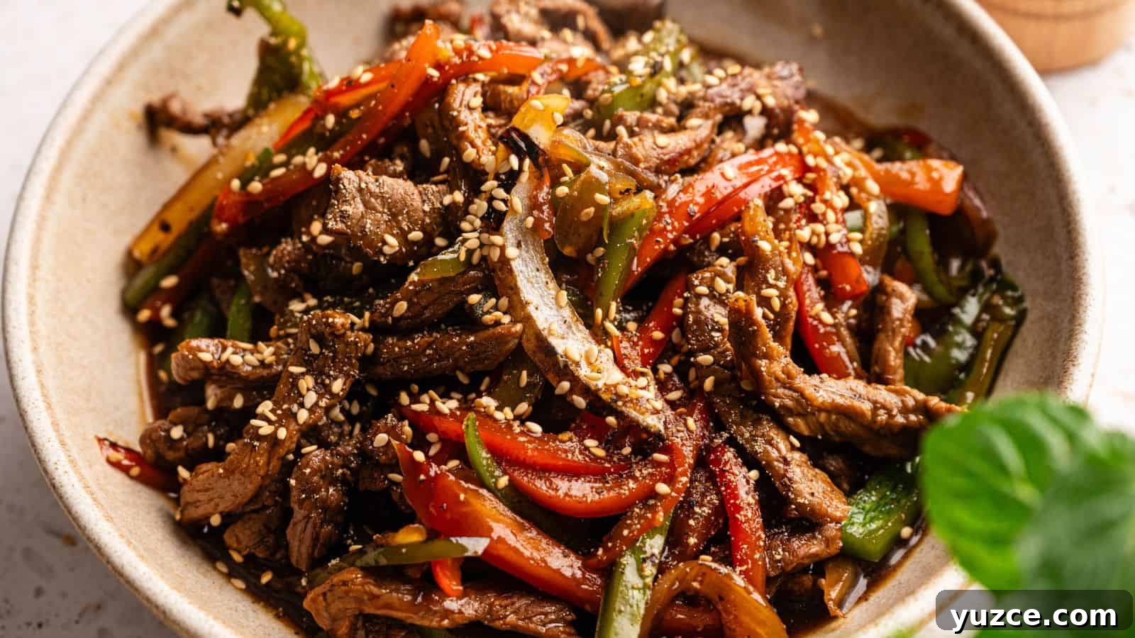A bowl of stir-fried beef strips with red and green bell peppers, topped with sesame seeds.