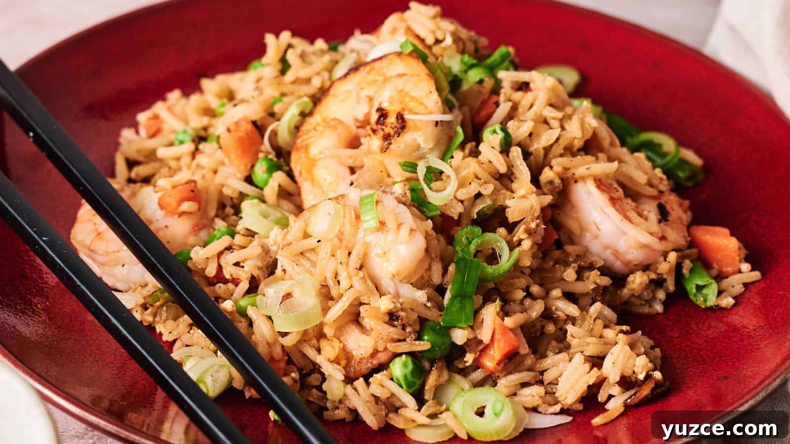 A red plate of shrimp fried rice garnished with chopped green onions, with black chopsticks resting on the side.