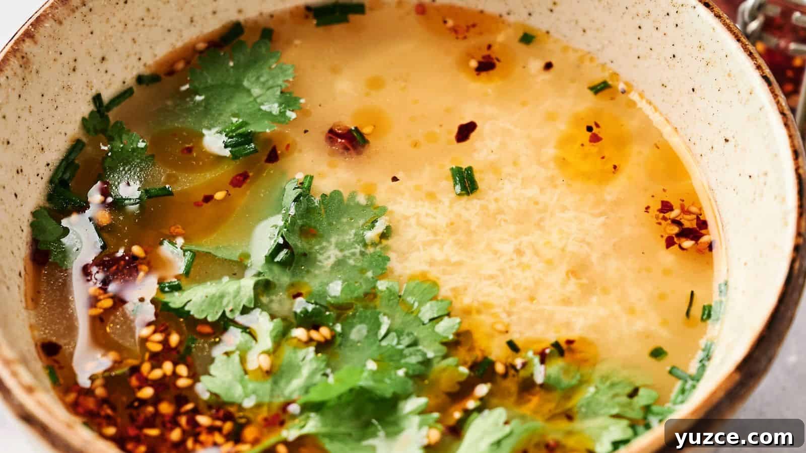 A comforting bowl of egg drop soup elegantly garnished with fresh cilantro, vibrant chives, and a sprinkle of chili flakes.