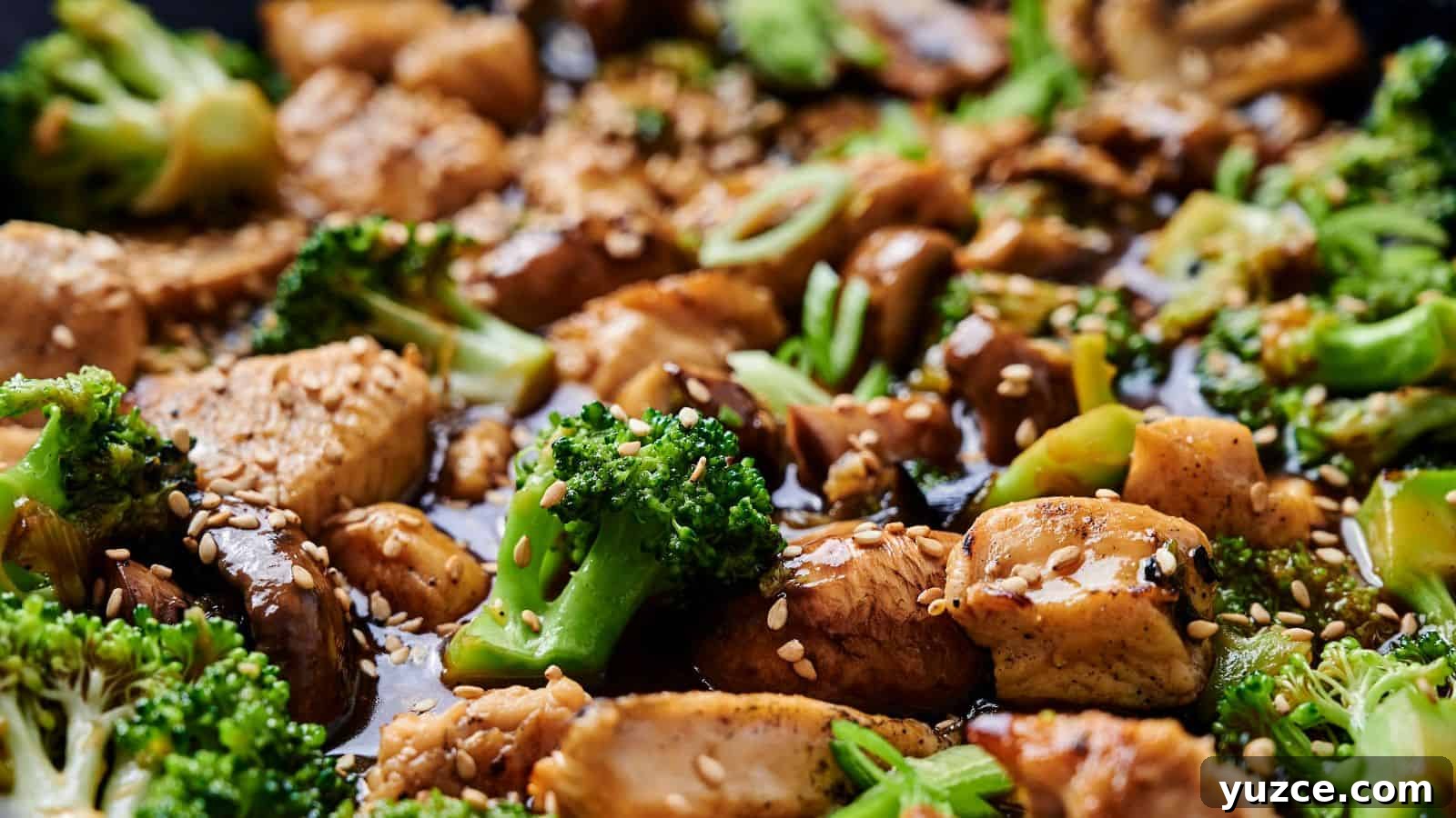 Close-up of a stir-fry dish with chicken, broccoli, mushrooms, and sesame seeds, coated in a soy-based sauce.