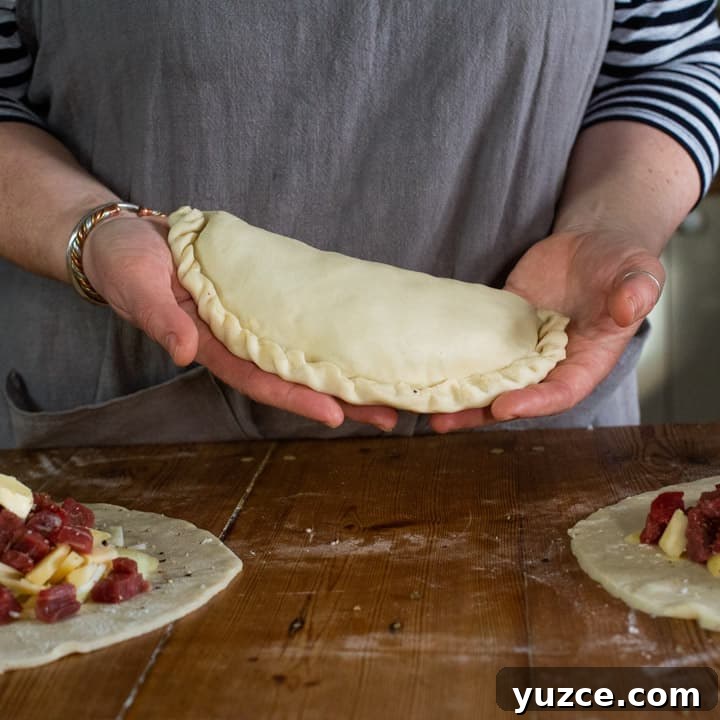 Authentic Cornish Pasty Recipe: Traditional Step-by-Step Guide 13 womans hands holding an uncooked, homemade pasty that is ready to be baked