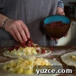 Authentic Cornish Pasty Recipe: Traditional Step-by-Step Guide 18 three discs of pastry on a wooden surface, piled up with raw swede, potato, onion and steak ready to be crimped into pasty's