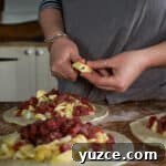 Authentic Cornish Pasty Recipe: Traditional Step-by-Step Guide 19 womans hands chopping a piece of butter up over the top of three pasties that are about to be crimped