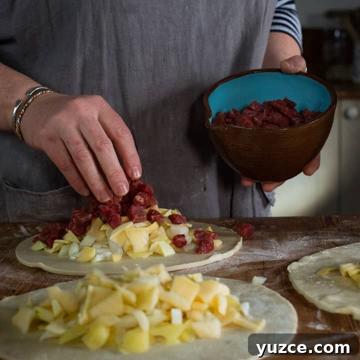 Authentic Cornish Pasty Recipe: Traditional Step-by-Step Guide 8 three discs of pastry on a wooden surface, piled up with raw swede, potato, onion and steak ready to be crimped into pasty's