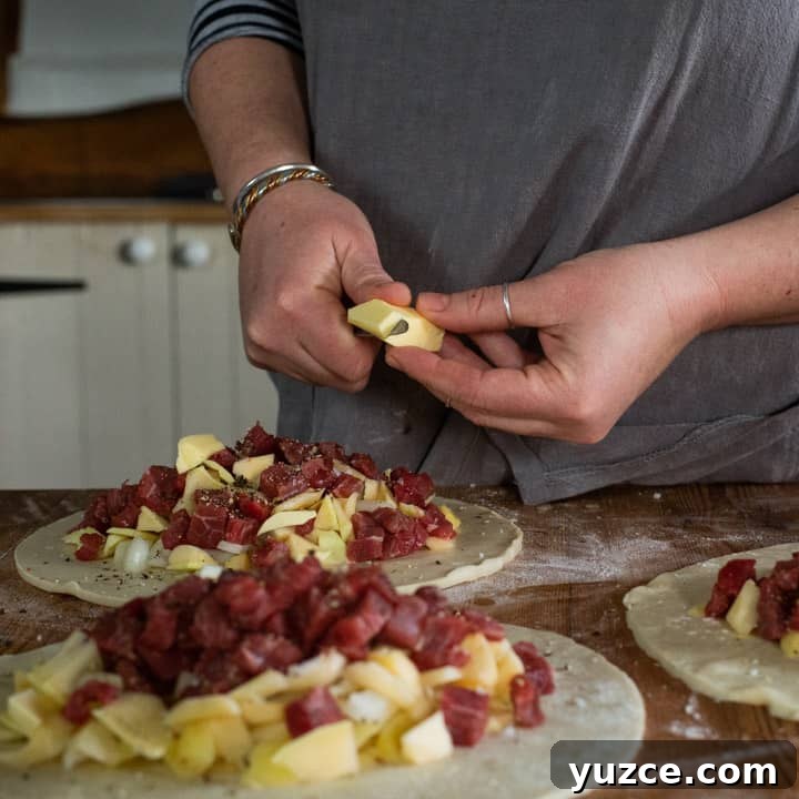 Authentic Cornish Pasty Recipe: Traditional Step-by-Step Guide 9 womans hands chopping a piece of butter up over the top of three pasties that are about to be crimped
