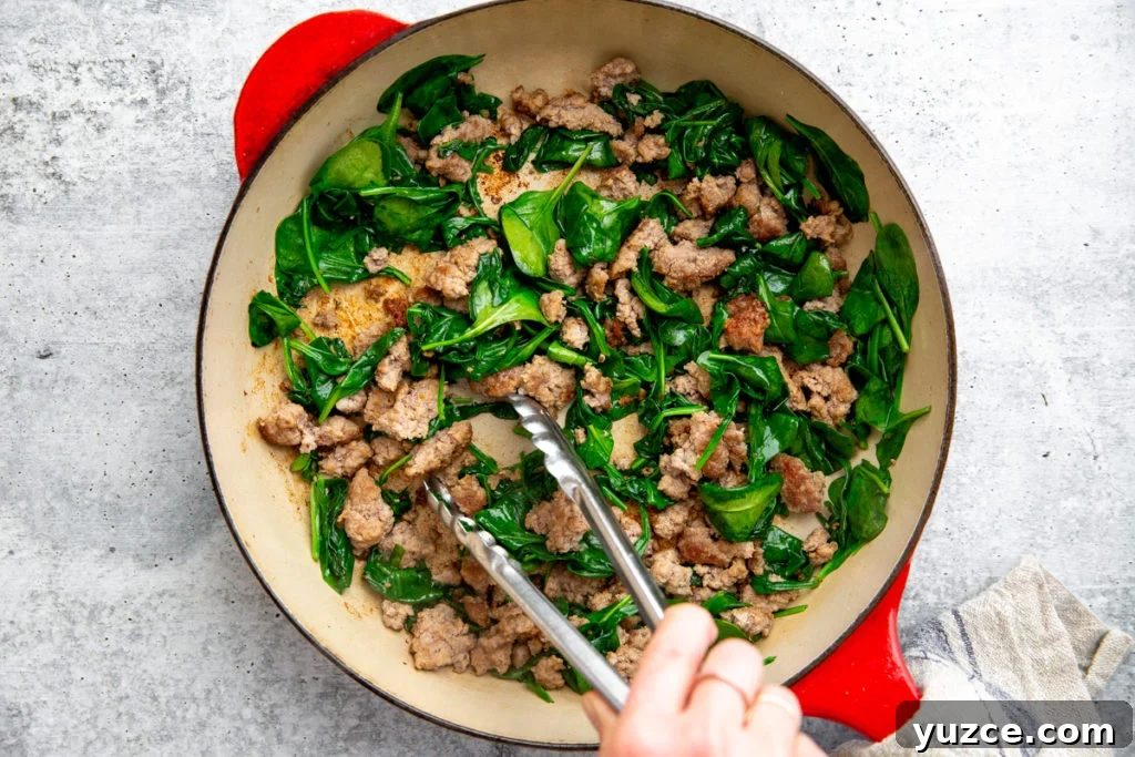 Spicy Peanut Pork Noodles (Gluten-Free, Ready in Minutes) 9 A hand stirring spinach into the skillet with the cooked pork.