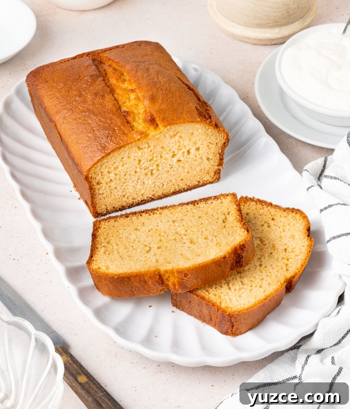 Classic French Yogurt Cake (Gâteau au Yaourt) Recipe 4 Cake on a white tray with two slices stacked at the front.