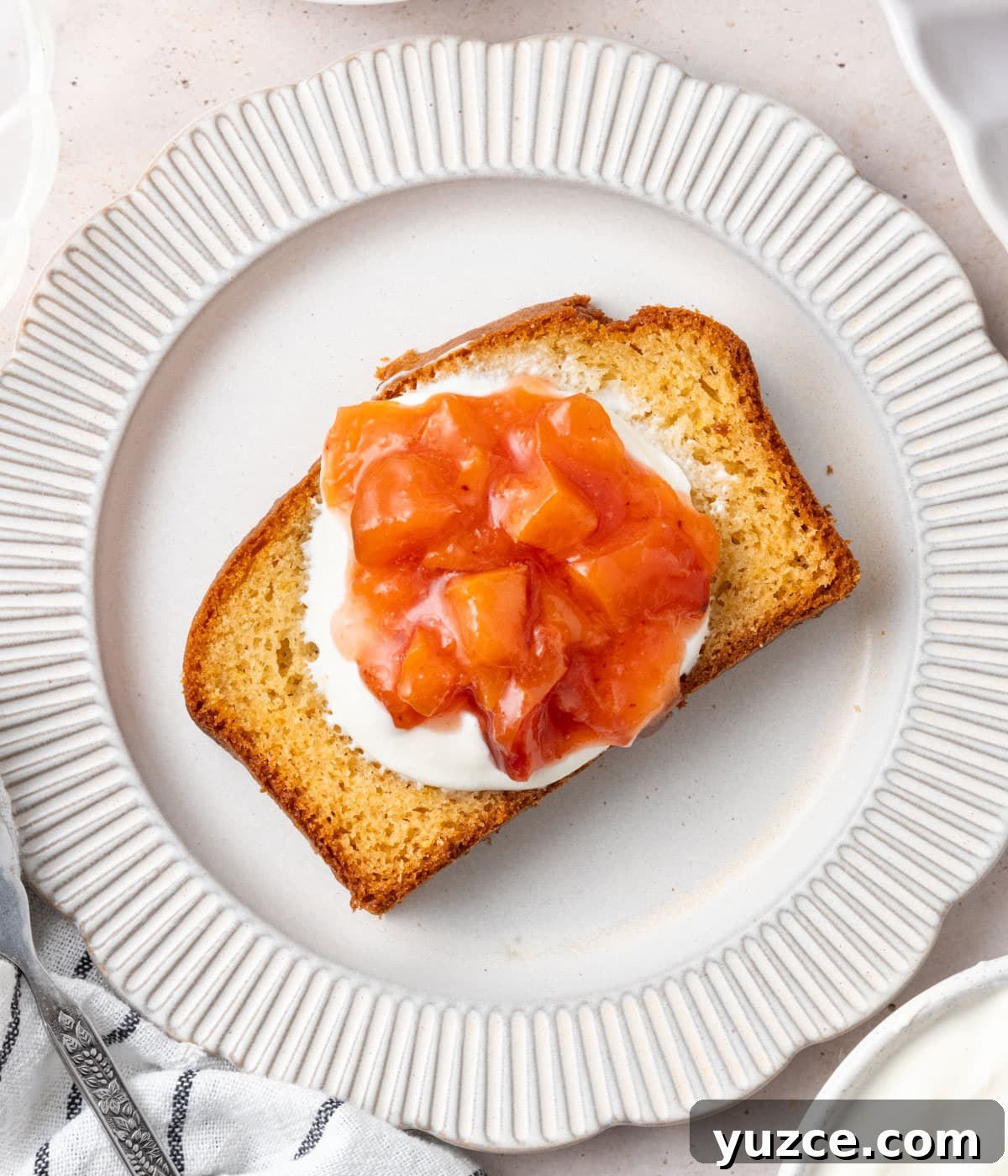 Classic French Yogurt Cake (Gâteau au Yaourt) Recipe 8 A slice of cake topped with yogurt and peach compote seen from above on a small white plate.