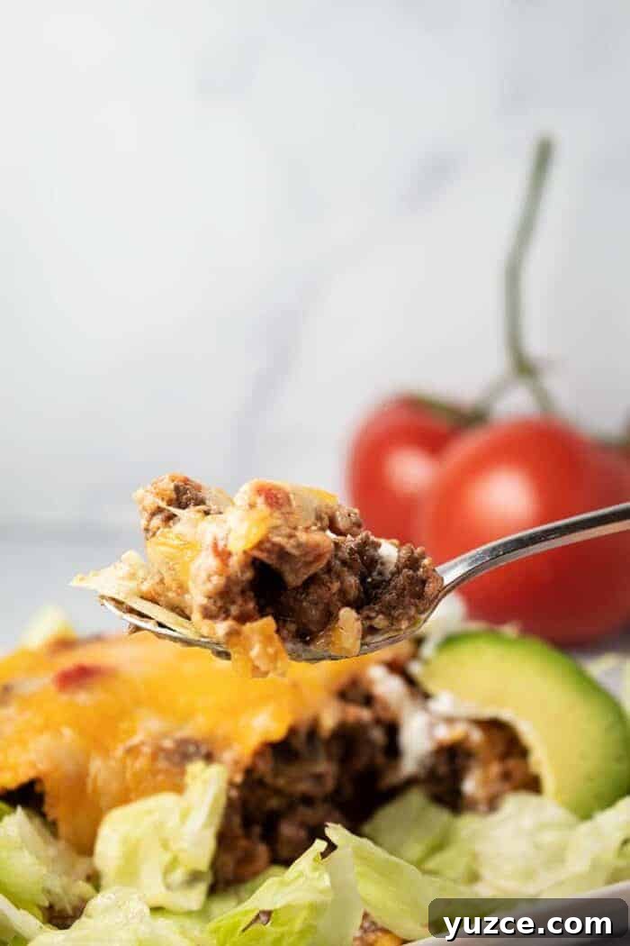 spoon full of beef held up in front of keto taco casserole with lettuce and avocado