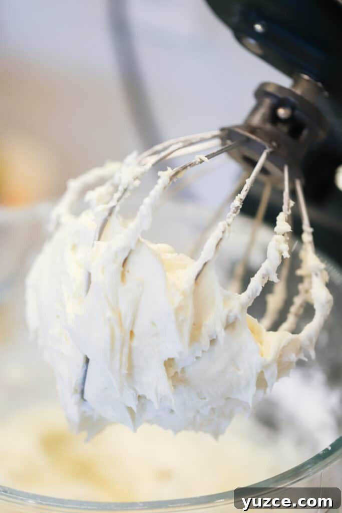 Homemade cream cheese icing on a wire whisk.