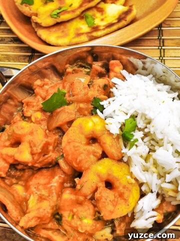 Kashmiri chicken and prawn curry in a dish in front of a plate of homemade buttered naan bread.