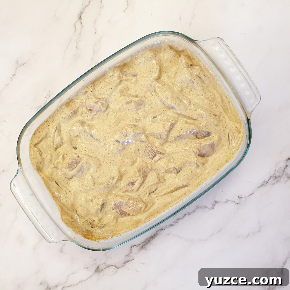 Creamy Murgh Makhani (Authentic Butter Chicken Recipe) 6 A glass dish filled with chicken pieces marinating in a butter curry sauce.