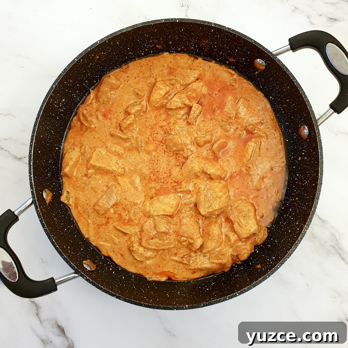 Creamy Murgh Makhani (Authentic Butter Chicken Recipe) 10 A frying pan containing pieces of chicken breast in a buttery tomato curry sauce.