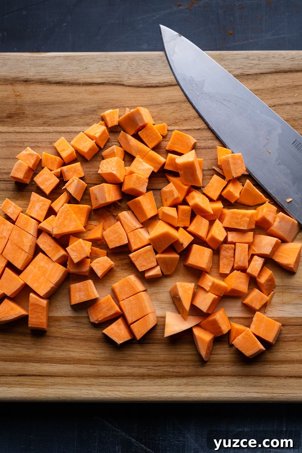 Hearty Sweet Potato and Black Bean Chili Recipe 4 Diced pieces of sweet potato on a wooden cutting board with a knife next to it.