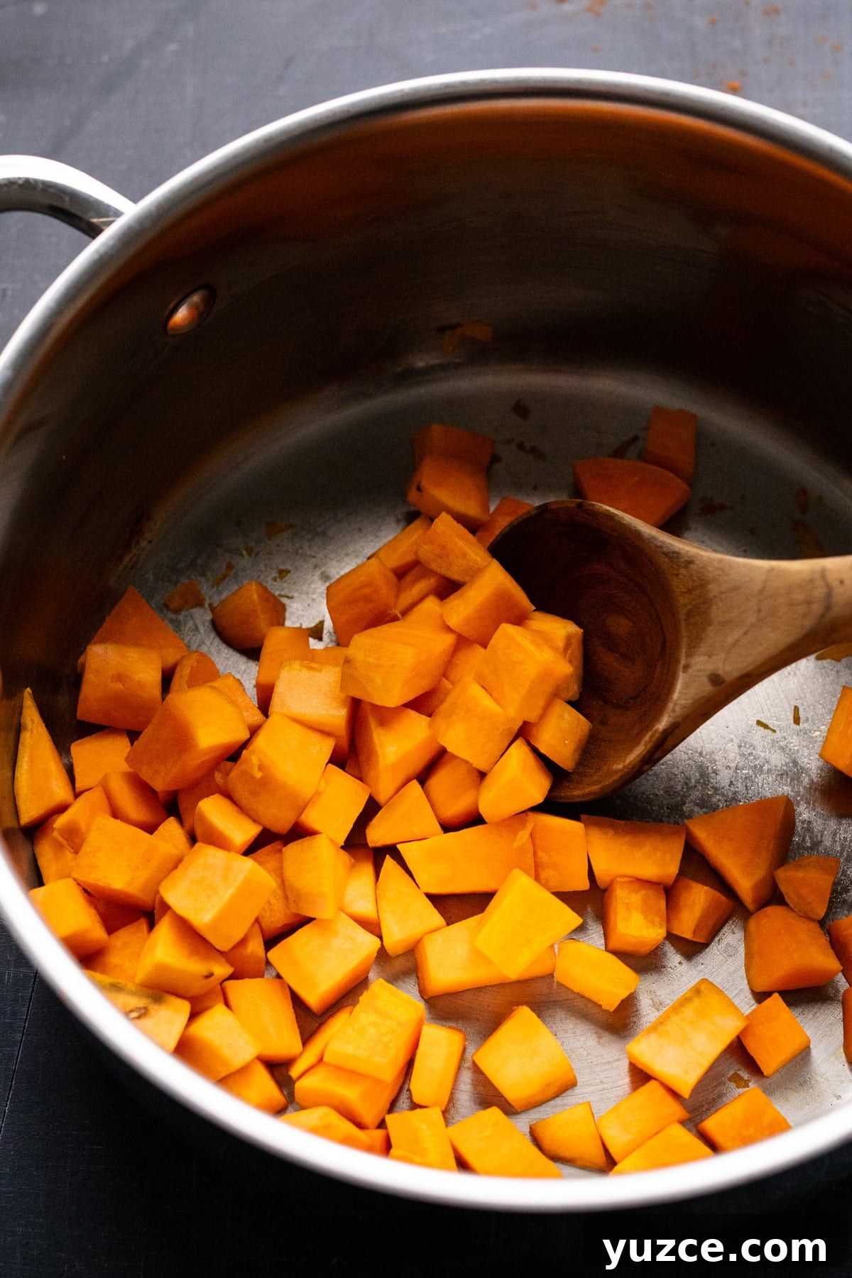Hearty Sweet Potato and Black Bean Chili Recipe 5 Diced pieces of sweet potato being sautéed in a stainless steel pot with a wooden spoon.