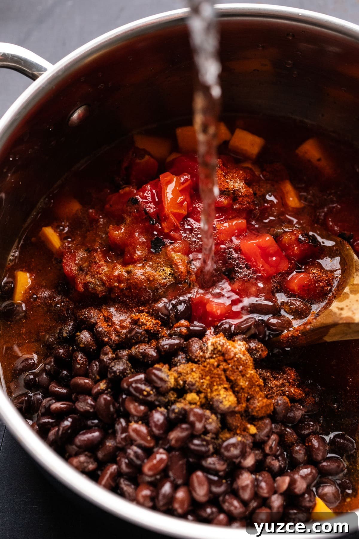 Hearty Sweet Potato and Black Bean Chili Recipe 6 Ingredients for sweet potato chili in a pot with water being poured into it.