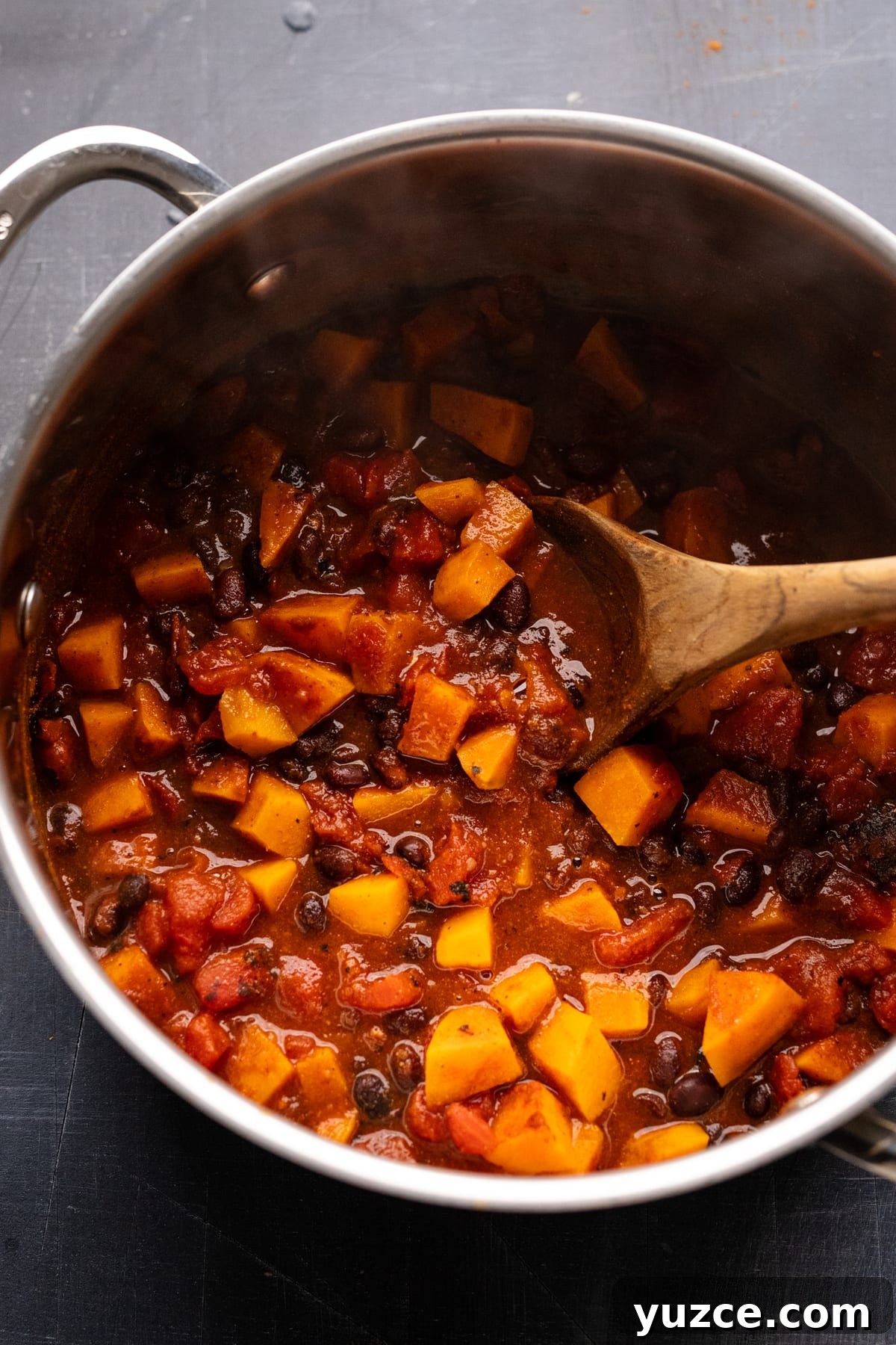 Hearty Sweet Potato and Black Bean Chili Recipe 7 Sweet potato black bean chili being stirring in a pot with a wooden spoon.