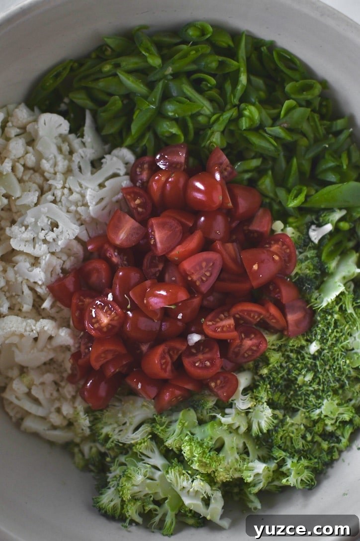 Crisp Snap Pea Salad with Lemon-Herb Vinaigrette 4 peas, broccoli, cauliflower, and tomatoes cut up ready to be tossed with dressing.