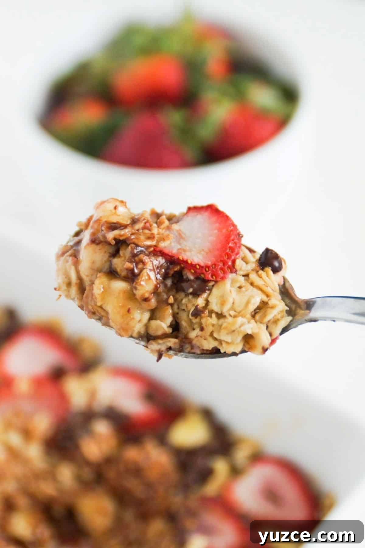 Banana and strawberry baked oatmeal on a spoon up close, with the rest in a serving dish in the background.