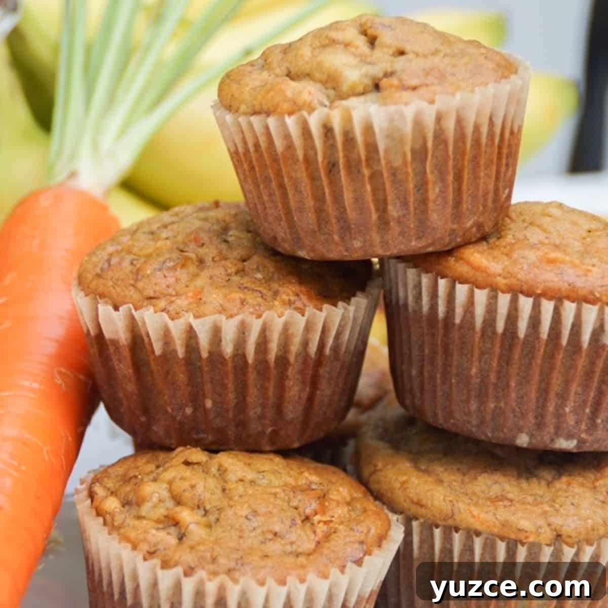 Stack of banana carrot muffins with a carrot and bananas in the background.