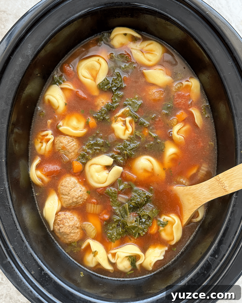 overhead shot of cooked Meatball Tortellini Soup in a black slow cooker