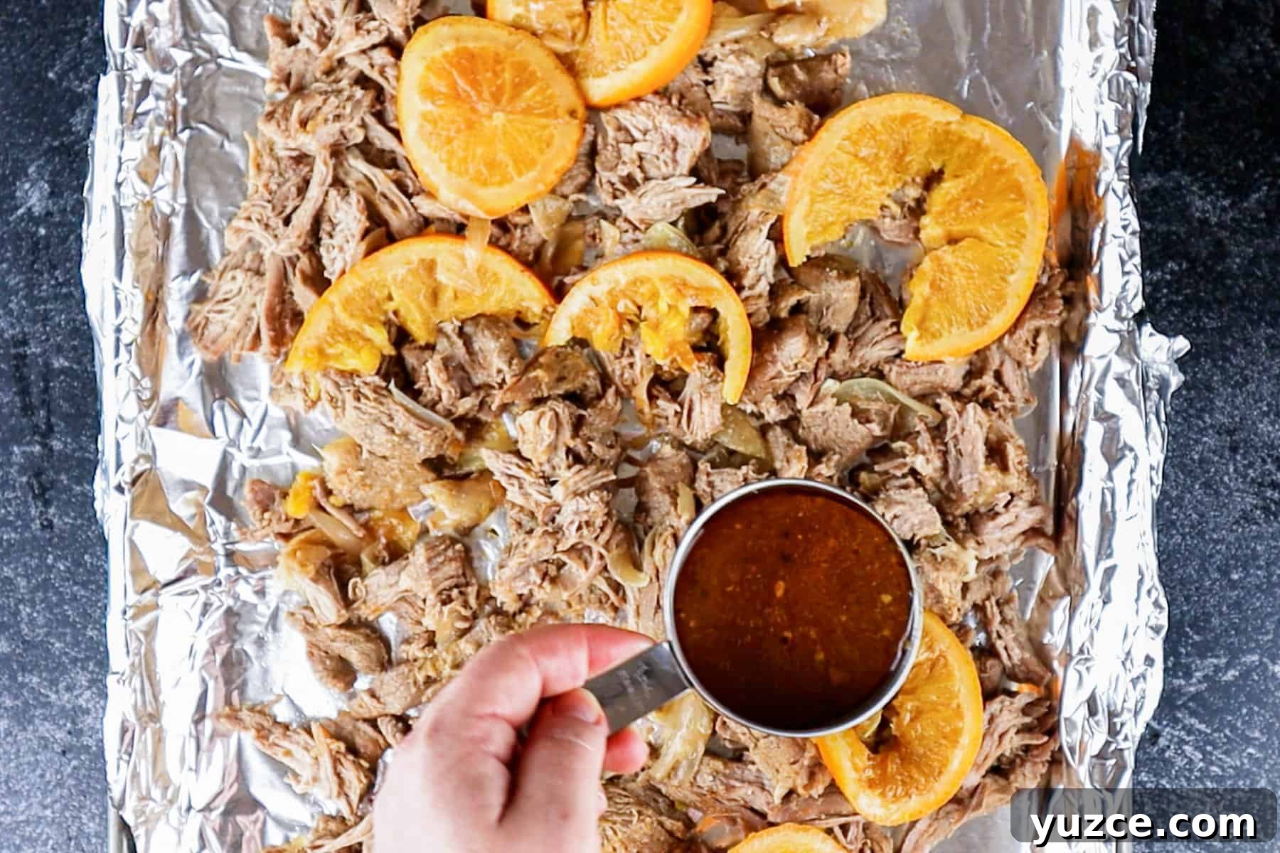 Authentic Pork Carnitas Street Tacos Recipe 8 Pouring broth over shredded pork on foiled lined baking sheet.
