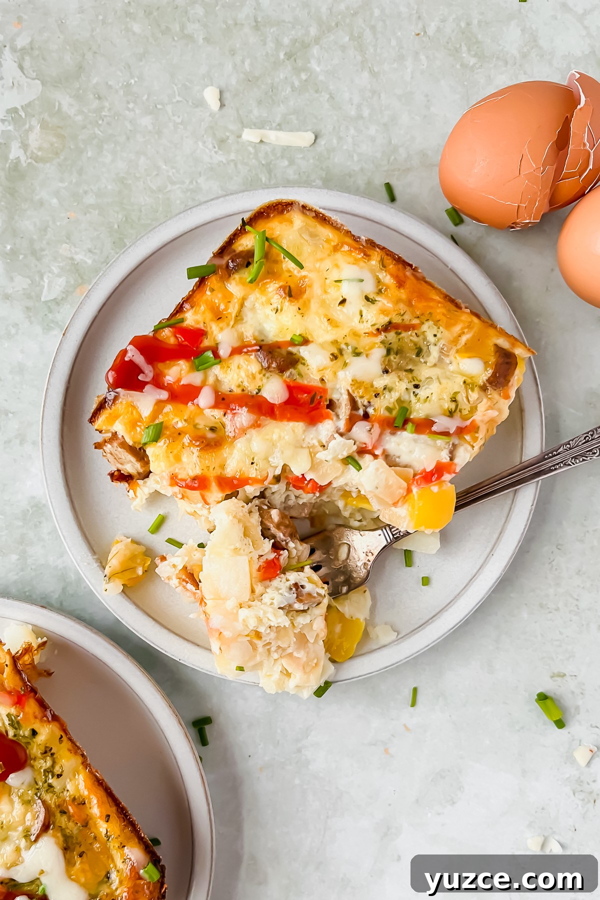 Ultimate Cheesy Loaded Hashbrown Casserole Recipe 2 slice of loaded hashbrown casserole on white serving plate beside egg shells.