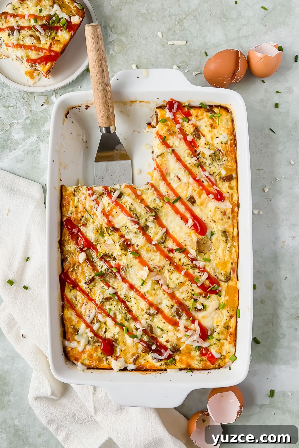 Ultimate Cheesy Loaded Hashbrown Casserole Recipe 11 baked loaded hashbrown casserole in white baking dish drizzled with ketchup with slice taken out and put on plate