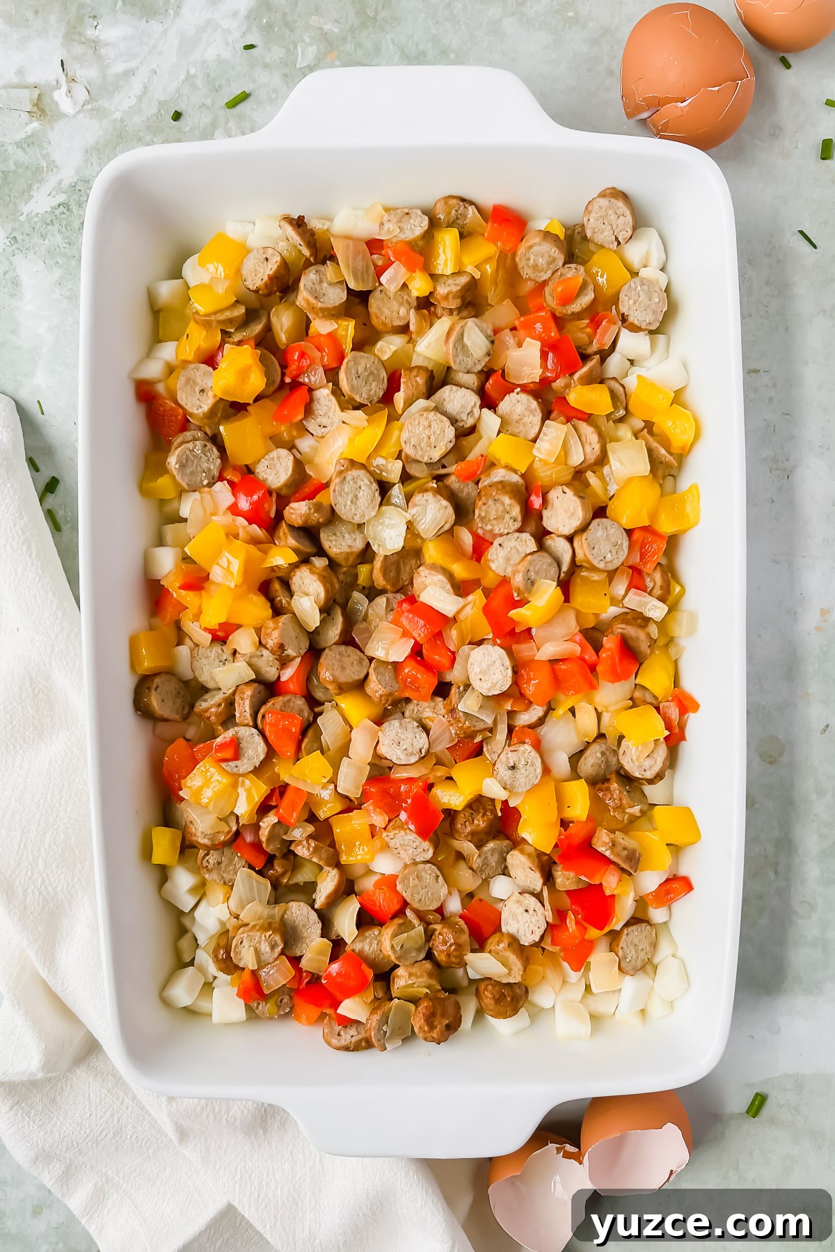 Ultimate Cheesy Loaded Hashbrown Casserole Recipe 7 potatoes, peppers, and sausage in white rectangular baking dish.