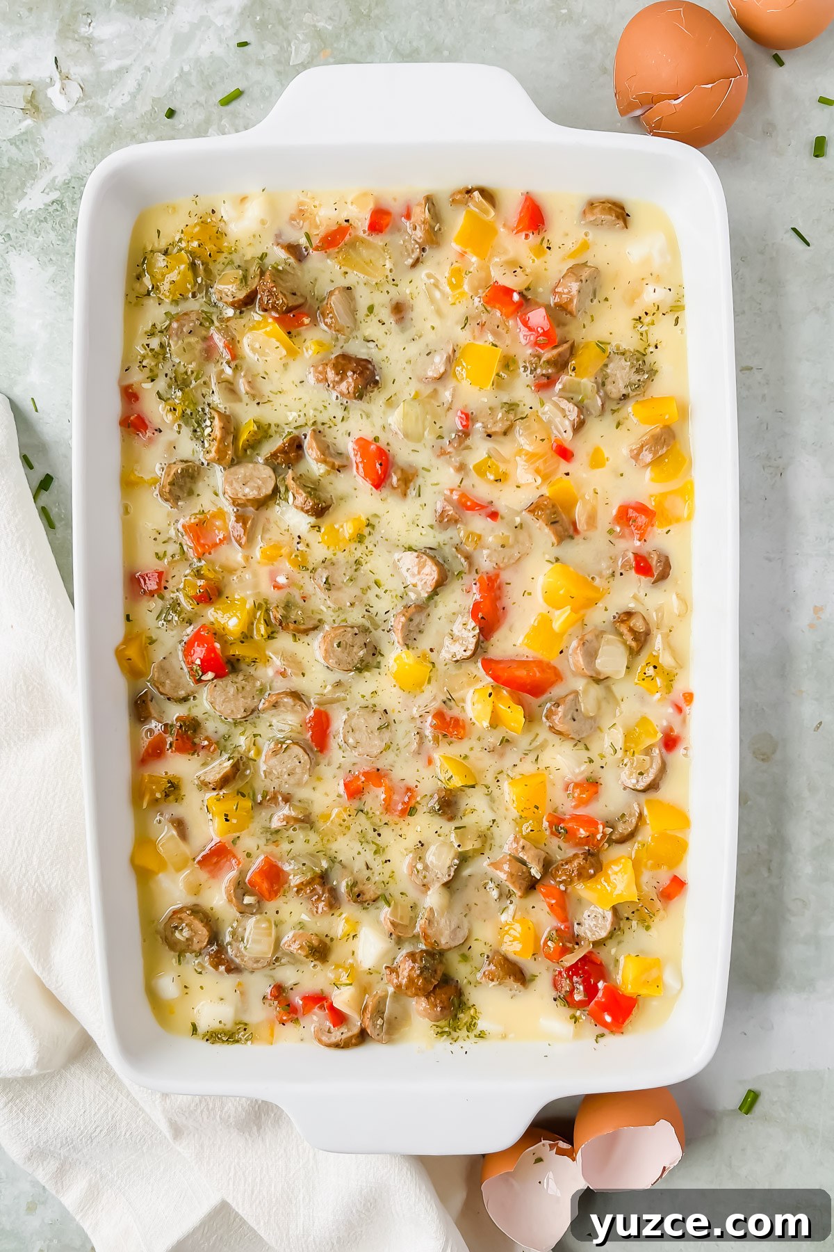 Ultimate Cheesy Loaded Hashbrown Casserole Recipe 8 raw loaded hashbrown casserole topped with seasonings in white rectangular baking dish.