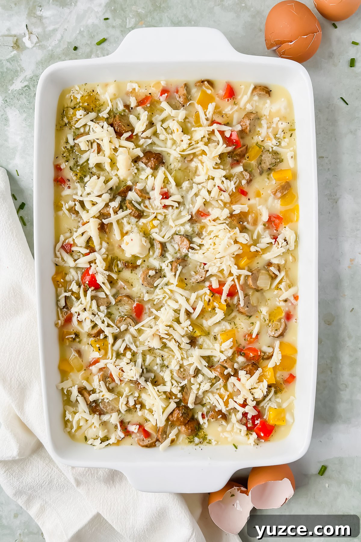 Ultimate Cheesy Loaded Hashbrown Casserole Recipe 9 raw loaded hashbrown casserole topped with shredded cheese in white rectangular baking dish.