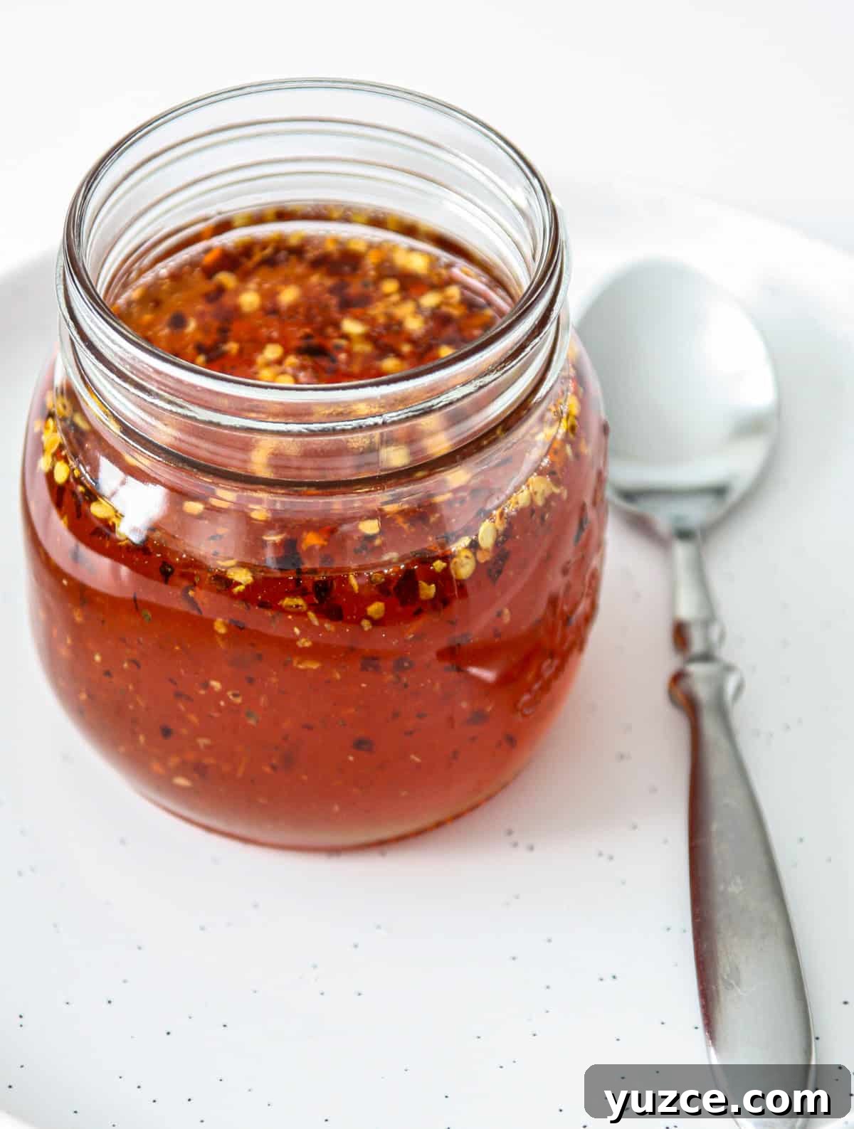 Homemade Hot Honey Recipe for Spicy-Sweet Drizzling and Cooking 2 Hot honey in a glass jar next to a silver spoon.