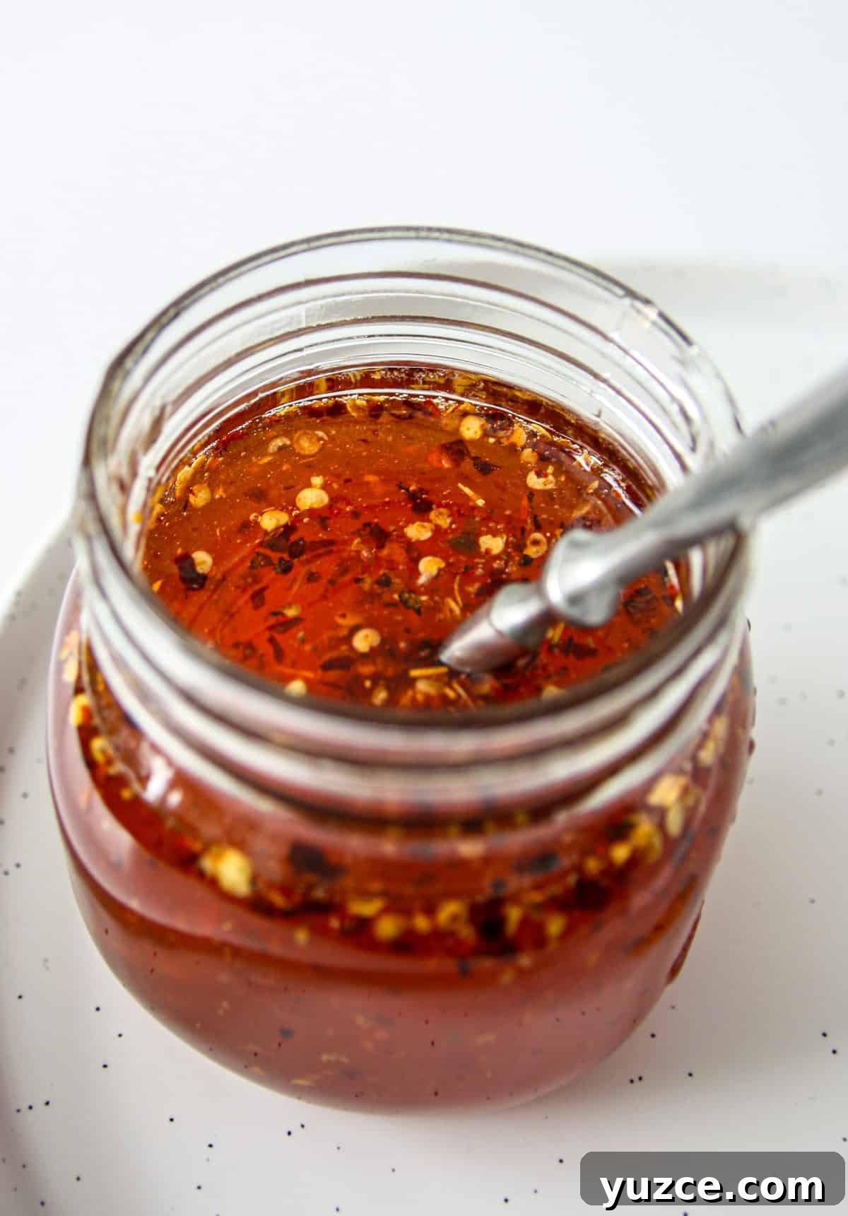 Homemade Hot Honey Recipe for Spicy-Sweet Drizzling and Cooking 5 Hot honey sauce in a glass jar with a spoon inserted.
