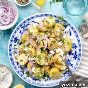 Perfect Reverse Sear Steak Technique for Tender, Crispy Results 11 A bowl of Greek potato salad with red onions, feta cheese, herbs, and capers on a blue-patterned plate, surrounded by lemon, salt, pepper, oil, and a striped serviette on a blue table.