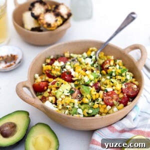 Perfect Reverse Sear Steak Technique for Tender, Crispy Results 13 A bowl of grilled corn avocado salad with cherry tomatoes, feta, and herbs sits on a white table. Nearby are a halved avocado, lime, grilled corn slices, a drink, and a vase with yellow flowers.
