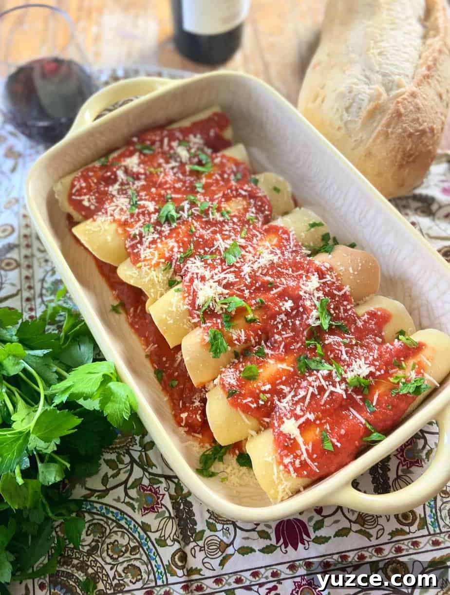 Three-Cheese Manicotti Crepes: Stuffed Italian Recipe 2 Manicotti crepes in a yellow baking dish with marinara sauce, grated parmesan cheese and fresh parsley on top.