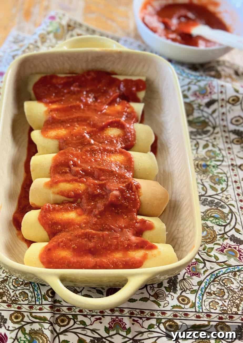 Three-Cheese Manicotti Crepes: Stuffed Italian Recipe 8 Manicotti in baking dish topped with red pasta sauce.