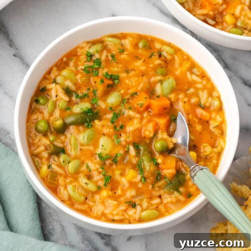 A spoon scooping a bite of vegetable rice soup from a serving bowl.
