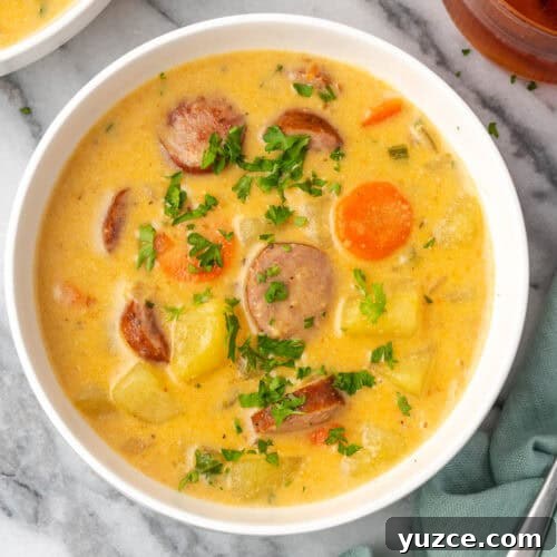 A bowl of kielbasa potato soup sitting on a marble counter.