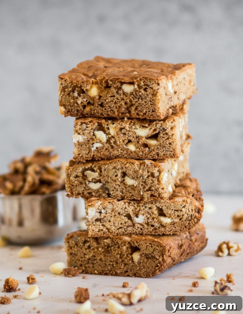 Gluten-Free White Chocolate Blondies Recipe for Chewy, Fudgy Bars 2 gluten free white chocolate blondies cut into square bars and stacked on each other with walnuts and white chocolate chips spread around them
