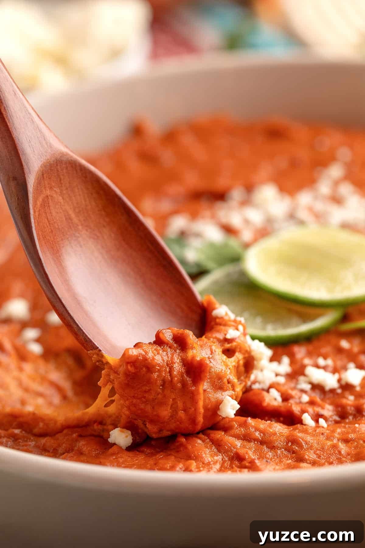 Chipotle Chorizo Bean Dip Recipe — Smoky Spicy Party Dip 9 Wooden spoon scooping creamy chorizo bean dip, showing its thick, smooth texture with crumbled cheese and lime slices in the background.