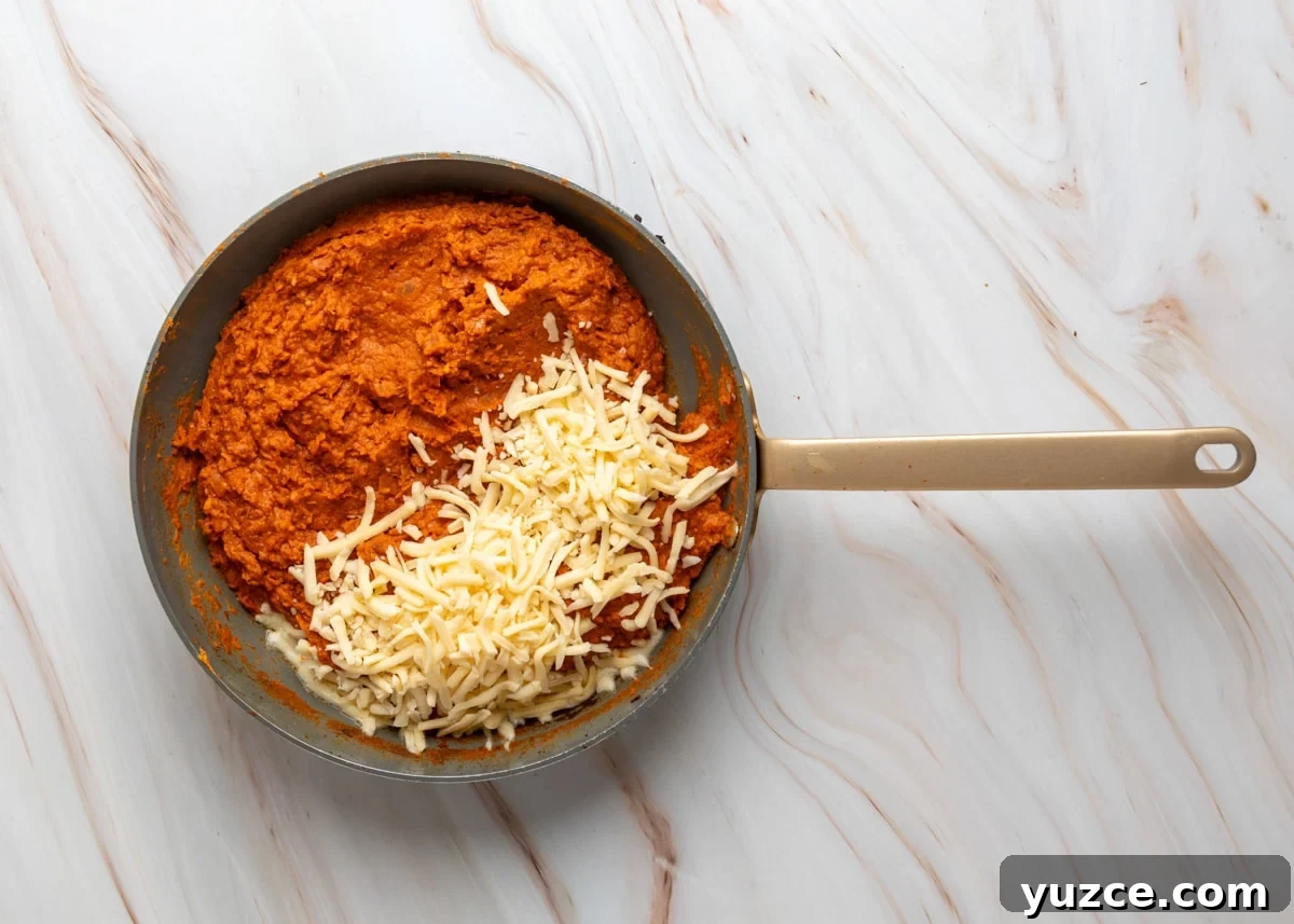 Chipotle Chorizo Bean Dip Recipe — Smoky Spicy Party Dip 7 Overhead view of blended chorizo bean mixture in a skillet with shredded cheese added on top, ready to melt.