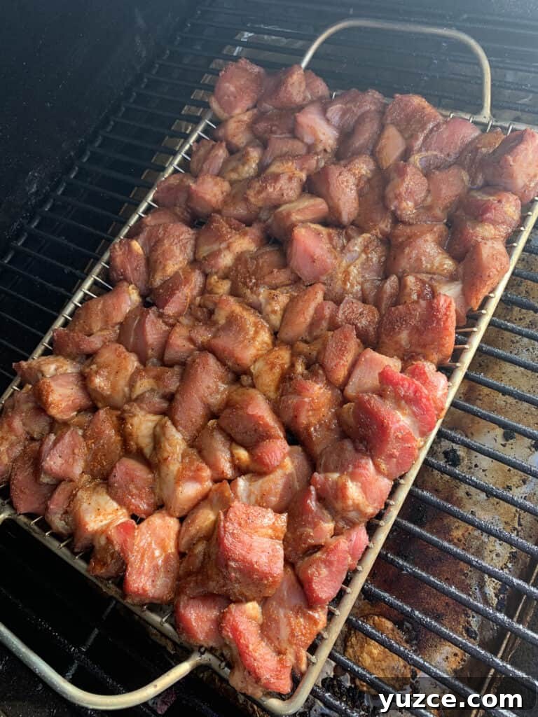 Smoky Pork Shoulder Burnt Ends Recipe for Tender, Crispy Bites 3 Chunks of pork shoulder on a grilling rack in a smoker